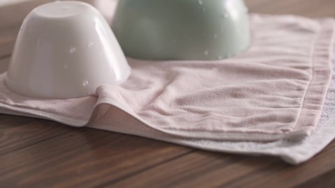 A woman's hand puts a wet plate on a towel. Clean bowls on a tea towel. Kitchen in elegant pastel colors. Three deep plates: white, pastel pink and pastel green. White and pink tea towel. Textured