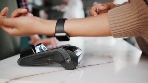 NFC banking technology. Close-up of young woman using smart watch credit card with NFC chip on bank terminal. Customer paying for food or coffee in restaurant or cafe, small business