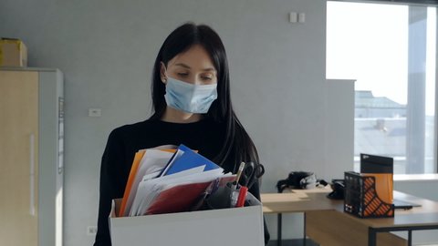 Young woman wearing mask holding box of personal belongings leaving office after losing job economic crisis and unemployment during covid-19 epidemic. Slow motion