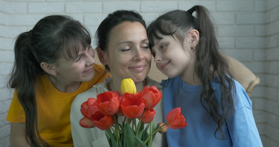 Greeting with mother flowers at home. Two daughter with mother celebrace birthday with a bouquet of tulips. Mother