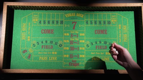 Burbank, CA USA - May 11 2021: This wide angle video shows a gambler's hand rolling a pair of dice on a retro craps table in slow motion.