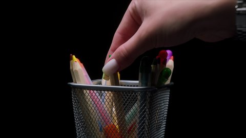 Close-up of colored pencils and markers in a metal grey basket, shooting stationery on black background, pencil stand.