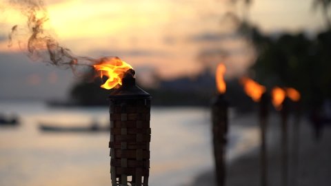 Flame form tiki torch at sunset with silhouette of palm tree in slow motion. Vacation and travel concept.