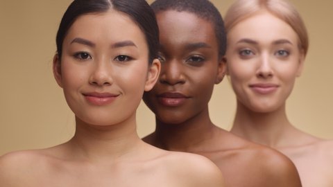 Spa and body care concept. Beauty portrait of three diverse beautiful ladies smiling to camera, standing one by one over beige studio background