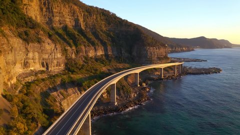 Curvy Sea Cliff Bridge Road, A View Of Majestic Mountains And Clear Blue Waters Of Tasman Sea In NSW Australia - aerial shot
