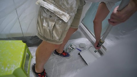 Painter Dipping Paint Roller In Paint Pan In Bathroom Covered In Plastic 