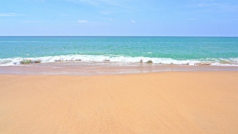 Static shot of the ocean with calm waves reaching the shore of a white sand beach on a tropical island during bright sunny day.