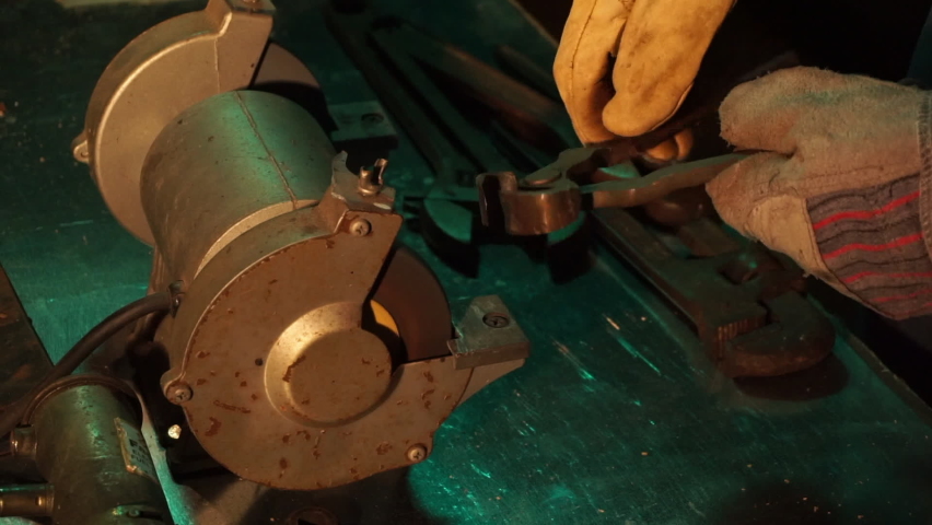 Slow motion of tool sharpened on bench grinder. Star-shaped sparks are reflected in metal surface of workbench.