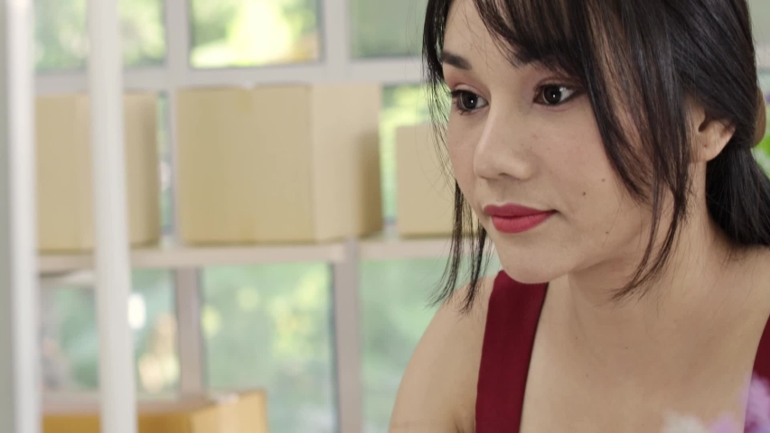 Asian brunette black hair red shirt and red lips looking at computer or laptop screen typing and smiling