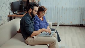Happy Senior Woman Watch Internet Websites With Son.Family Relationship Online Chatting Social Network.Happy Older Parent Mother And Adult Grown Son Sit On Sofa.Millennial Son Watching Video On Laptop