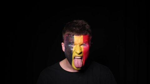 Happy football fan celebrate victory of his favourite team Belgium. Young man with face painted in national colours of Belgian Flag. Portrait of young man supports his national team at home