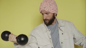 Bearded man in pink hat training his mental health with brain lifting black dumbbells, 4k video.
Funny diy knitted hat. Mindfulness practice. Yellow background. Education mind sport. Self care 