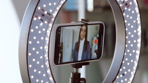 Young business woman writing vlogging by smartphone. A blogger girl takes pictures on the phone using a ring lamp. Video de stock