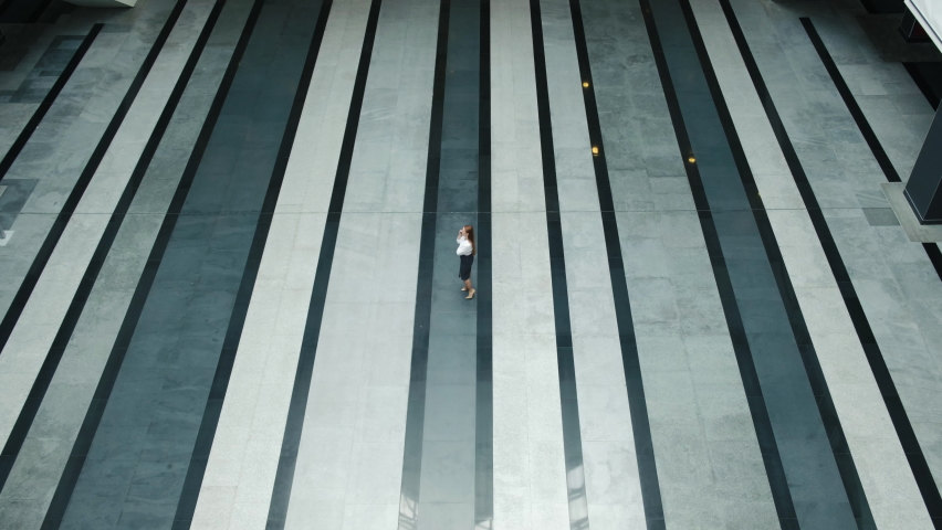 Attractive young businesswoman leader walks through a large empty lobby of a business center with a phone. successful independent woman with a career development of the CEO of the company. top view