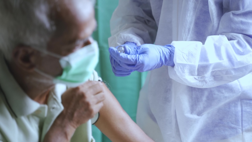 Senior elderly patient with mask getting vaccination or jab at hospital - Doctor in protective Hazmat suit treating Covid patient injecting anti-viral vials at covid care Centre. | Shutterstock HD Video #1073201054