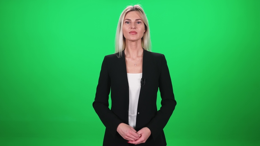 Woman reporter in suit looks into the camera and speaks in lavalier microphone, female on a green background, template for TV news agencies, journalist at work, chromakey.
