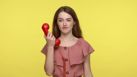 Contact us! Good looking brown haired woman in pink dress showing handset phone asking to call with flirting expressing, call center service. Indoor studio shot isolated on yellow background.