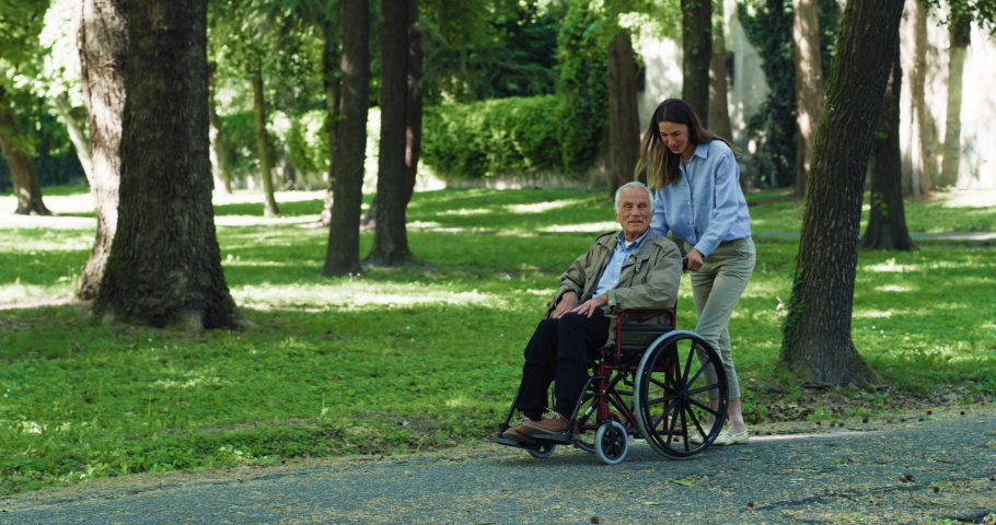 Cinematic shot of carefree happy granddaughter and grandfather who uses wheelchair having fun to walk together in green park. Concept of happiness, freedom, life, grandparents, generation,love, care Royalty-Free Stock Footage #1073215319