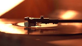Close up of a  tone arm and spinning vinyl record lit with warm red light.  Vinyl player music concept
