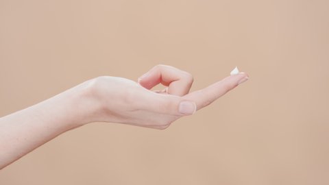 Female beauty model lifts her hand with a drop of moisturizer on forefinger up against beige ripple background | Moisturizer commercial