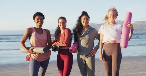 Portrait of group of diverse female friends holding yoga mats at the beach. healthy active lifestyle, outdoor fitness and wellbeing.
