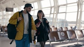 Happy couple of travellers with backpack walking together at airport lounge, using smartphones and talking. Young man and woman in stylish outfits travelling abroad. - Powered by Shutterstock - Get 15% off with code: PIKWIZARD15