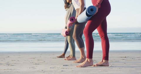 Group of diverse female friends preparing yoga mats before practicing yoga at the beach. healthy active lifestyle, outdoor fitness and wellbeing.
