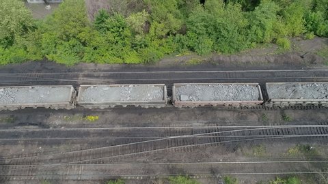 Railroad dump cars loaded with iron ore move from left to right. A bird's eye view.