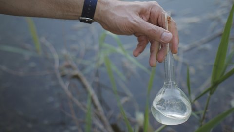 Men's Hand draws water from a polluted reservoir and holding test tube for analyzes with water on the background of the reservoir, the concept of water purity,