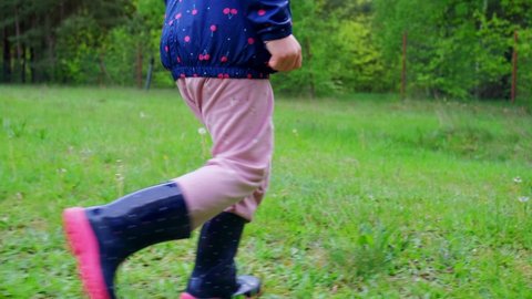
Caucasian Girl Wearing Wellington Gum Boots Walking and Running Through Grass Meadow Field