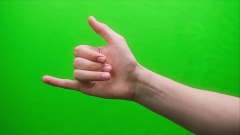 Close-up of a hand gesture shaka on a green background, shooting gesturing in studio.