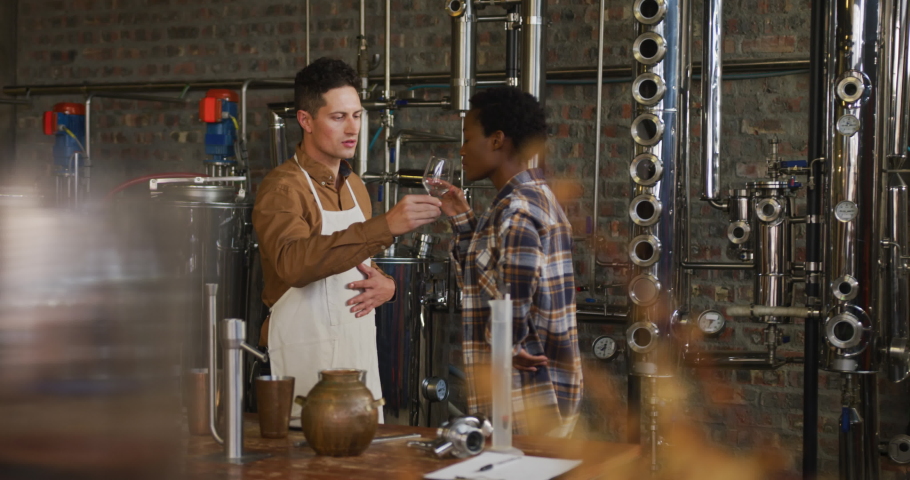 Diverse male and female colleague at gin distillery inspecting product, woman using tablet. work at an independent craft gin distillery business.