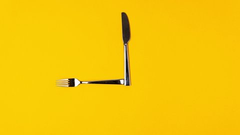 Time to eat, fork knife, alarm clock on yellow background. Stop motion animation, top view