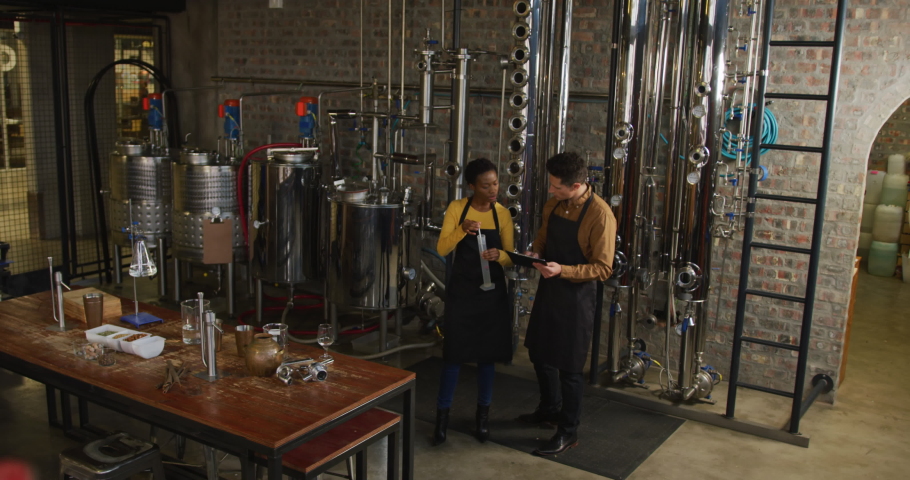 Diverse male and female colleague at gin distillery inspecting equipment, talking and making notes. work at an independent craft gin distillery business.