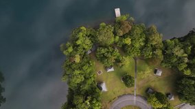Static drone video looking down on a lush park area next to a volcanic crater lake with clouds reflecting on the calm water