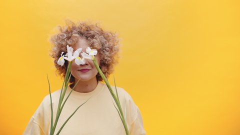 Funny young woman holding daffodils over her eyes and revealing her face with a smile