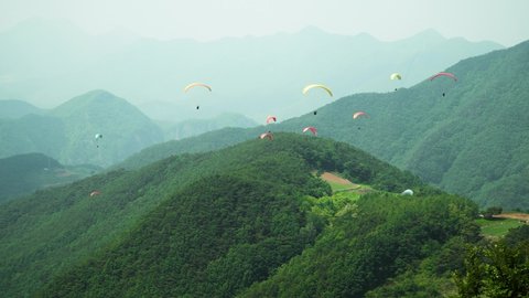 Paraglider taking off from the top of the hill and gliding towards many other people flying around green mountains in Danyang city, South Korea