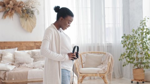 Afro american woman african black ethnic expectant mother listening to music song melody enjoying pregnancy dancing taking off headphones from head putting on pregnant belly audio therapy unborn baby