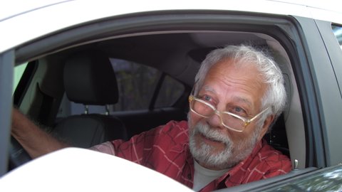 Drunk aged man with beard and glasses sits in automobile and talks with cheerful smile close view. Concept alcohol intoxication