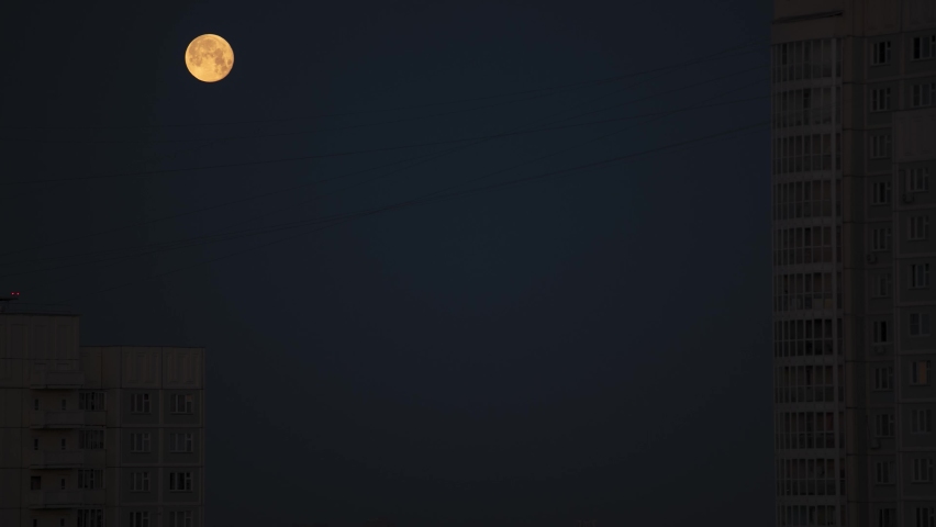 Full moon over the city. Time lapse of moon in the sky hiding behind high-rise buildings in the morning. Night to day transition