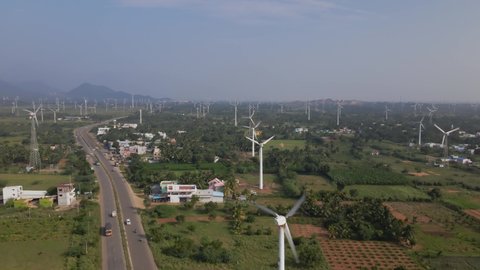 A landscape wide drone aerial moving shot of a two-lane busy roadway dividing huge farm of wind turbines on a bright sunny day in India. sustainable, clean, and renewable energy concept 
