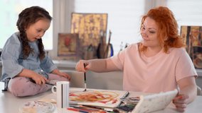 Mother helps her little daughter to do her creative drawing or spending time together concept. Caring caucasian mother shows daughter how to draw, cute girl gets amazed. 4k video footage