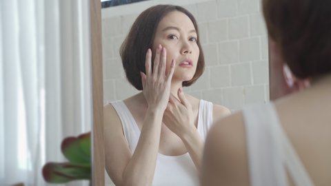 attractive beautiful short hair asian woman worry looking into mirror for face skin care condition. Frustrated Young female Examining Her Face While Looking At The Mirror in bathroom. annoy facial age