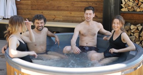 Company of friends bathing in outdoor jacuzzi or hot vat at the luxury spa. People relax have fun talking in wellness center