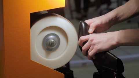 Shoemaker, shoes master using automatic orange shoe polish machine tool for polishing black leather women footwear at workshop - close up