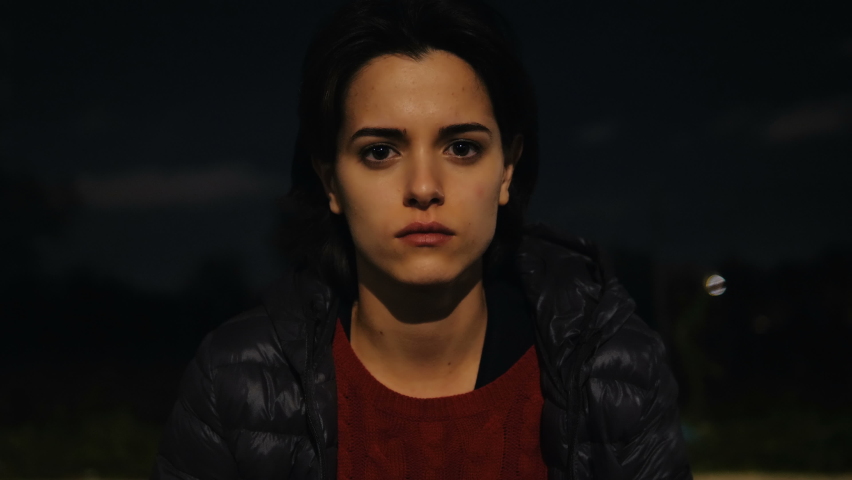 thoughtful young woman in the dark staring at camera dazzled by a sudden light