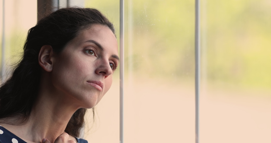 Close up head shot unhappy young hispanic latin caucasian woman looking out of window, feeling bored alone at home, suffering from solitude loneliness indoors, having psychological problems. Royalty-Free Stock Footage #1073278103
