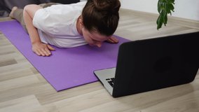 Online workout concept. Fit young woman doing yoga exercise, girl watching tv yoga class learning position with fitness tutorial on laptop computer stretching on mat at home, training body flexibility