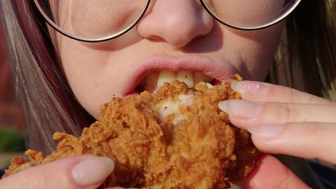 Young woman with glasses eating fried chicken . Fast food concept. Close up