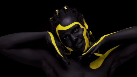 Face art. Dancing woman with black and yellow body paint. Young african girl with colorful bodypaint. An amazing afro american model with yellow makeup. Closeup face.